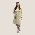 Beige cotton-blend knit dress for women with long sleeves, knee length (98–103 cm), front pocket and handmade flower applique on the side, available in sizes 36–52 and several colors: beige, dark blue and chocolate. Smėlinė trikotažinė suknelė su ilgarankovėmis, patogia kišene ir rankų darbo gėlyte, ilgis 98–103 cm, dydžiai 36–52, kelių spalvų pasirinkimas.