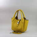Natūralios odos prancūziška maža rankinė ryškios geltonos spalvos, kompaktiškas modelis su trumpomis rankenomis ir ilga nusegama peties rankena, dekoratyvinė priekinė juostelė su metaliniu užsegimu, fotografuota ant šviesaus fono