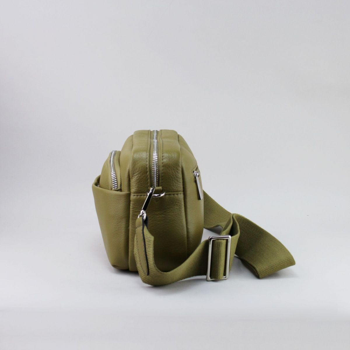 Side view of olive green leather handbag with double compartments and adjustable wide strap.
 Žalsvai alyvuogių odinės rankinės šoninis vaizdas su dviem skyriais ir plačiu reguliuojamu dirželiu.