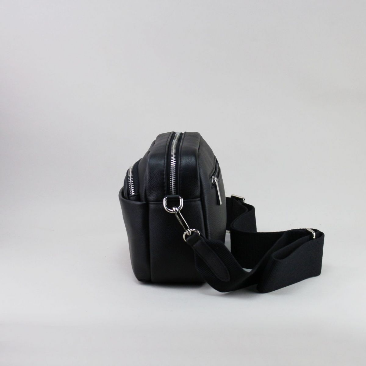 Side view of black leather handbag with structured design and detachable strap.
Juodos odinės rankinės šoninis vaizdas su tvirtu dizainu ir nusegamu dirželiu.