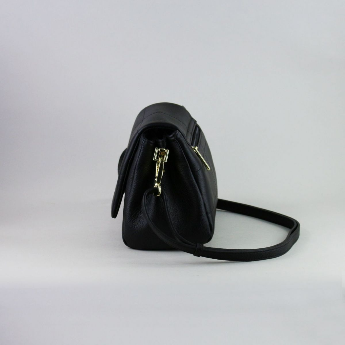 Black genuine leather handbag made by a reputable French manufacturer, featuring a structured flap closure, gold-tone hardware, rear zip pocket, and adjustable shoulder strap up to 115 cm. Elegant, compact, and timeless – a perfect accessory for daily use or evening outings. | Juoda natūralios odos rankinė, sukurta patikimo prancūzų gamintojo – su atvartu, auksine furnitūra ir reguliuojamu dirželiu – mėgstamas pasirinkimas stilingai moteriai.