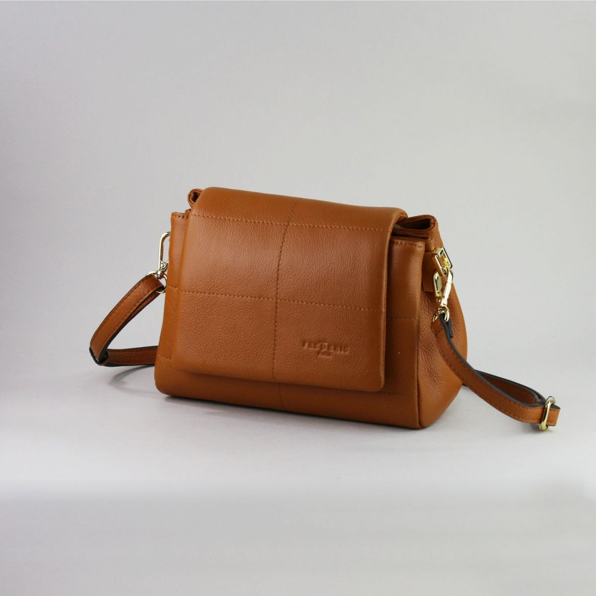 Caramel brown genuine leather handbag with flap closure, gold-tone hardware, adjustable shoulder strap (up to 115 cm), and exterior back zip pocket. Created by a trusted French manufacturer, this compact design is both elegant and practical – perfect for everyday or evening wear. | Karamelinės rudos spalvos natūralios odos rankinė su auksine furnitūra ir atvartu – stilingas ir mėgstamas modelis kasdienai ar išėjimui.

