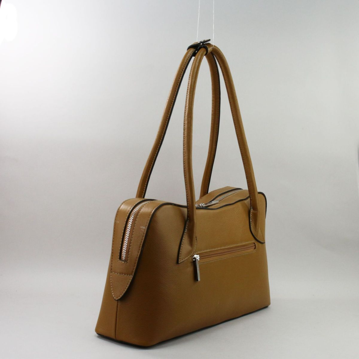 Side view of camel leather handbag with back zip pocket and detachable shoulder strap.
 Camel spalvos odinės rankinės šoninis vaizdas su galine kišene užtrauktuku ir nusegamu dirželiu.