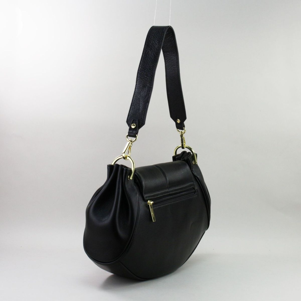 Black crescent-shaped genuine leather handbag with gold details and detachable strap.
 Juoda pusmėnulio formos natūralios odos rankinė su auksinėmis detalėmis ir nusegamu dirželiu.
