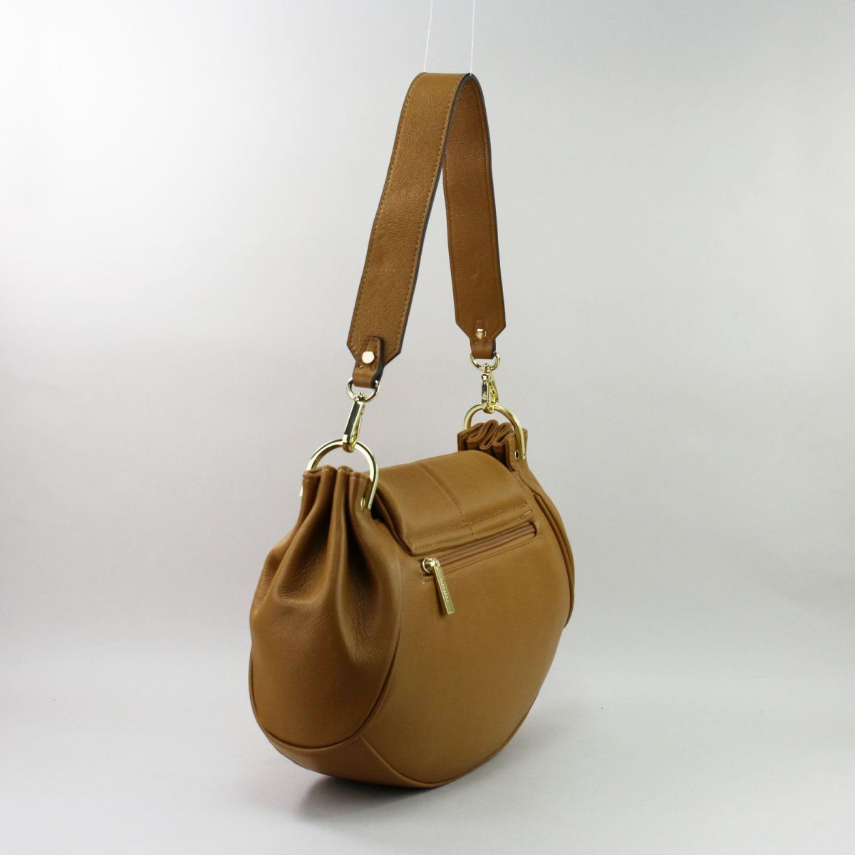 Back view of camel crescent leather handbag with rear zip pocket.
Camel spalvos pusmėnulio formos odinės rankinės nugarinė pusė su užtraukiama kišene.