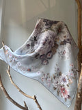 Luxury silk scarf with soft pastel floral print in shades of grey, lilac and beige. Square shape, 90x90 cm, made of 100% natural silk. Lightweight and breathable, perfect for wearing around the neck, shoulders, as a headscarf or tied to a handbag. A timeless fashion accessory and an elegant gift for her. – Prabangi šilkinė skarelė su švelniu pastelinių gėlių raštu pilkų, alyvinių ir rusvų tonų. Kvadratinė, 90x90 cm, iš 100 % natūralaus šilko. Lengva, kvėpuojanti, universaliai derinama.
