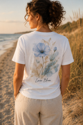 Balti moteriški ekologiškos medvilnės marškinėliai su mėlynos akvarelinės lino gėlės piešiniu, subtiliu Baltic Summer logotipu priekyje ir dideliu Linen Bloom dizainu nugaroje – minimalistinis vasariškas gamtos įkvėptas stilius.