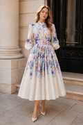 Elegantiška ilga moteriška suknelė su švelniu akvareliniu mėlynų, rožinių ir violetinių gėlių raštu, ilgomis pūstomis rankovėmis, skirtingomis dekoratyvinėmis sagutėmis ir liemenį pabrėžiančiu dirželiu.