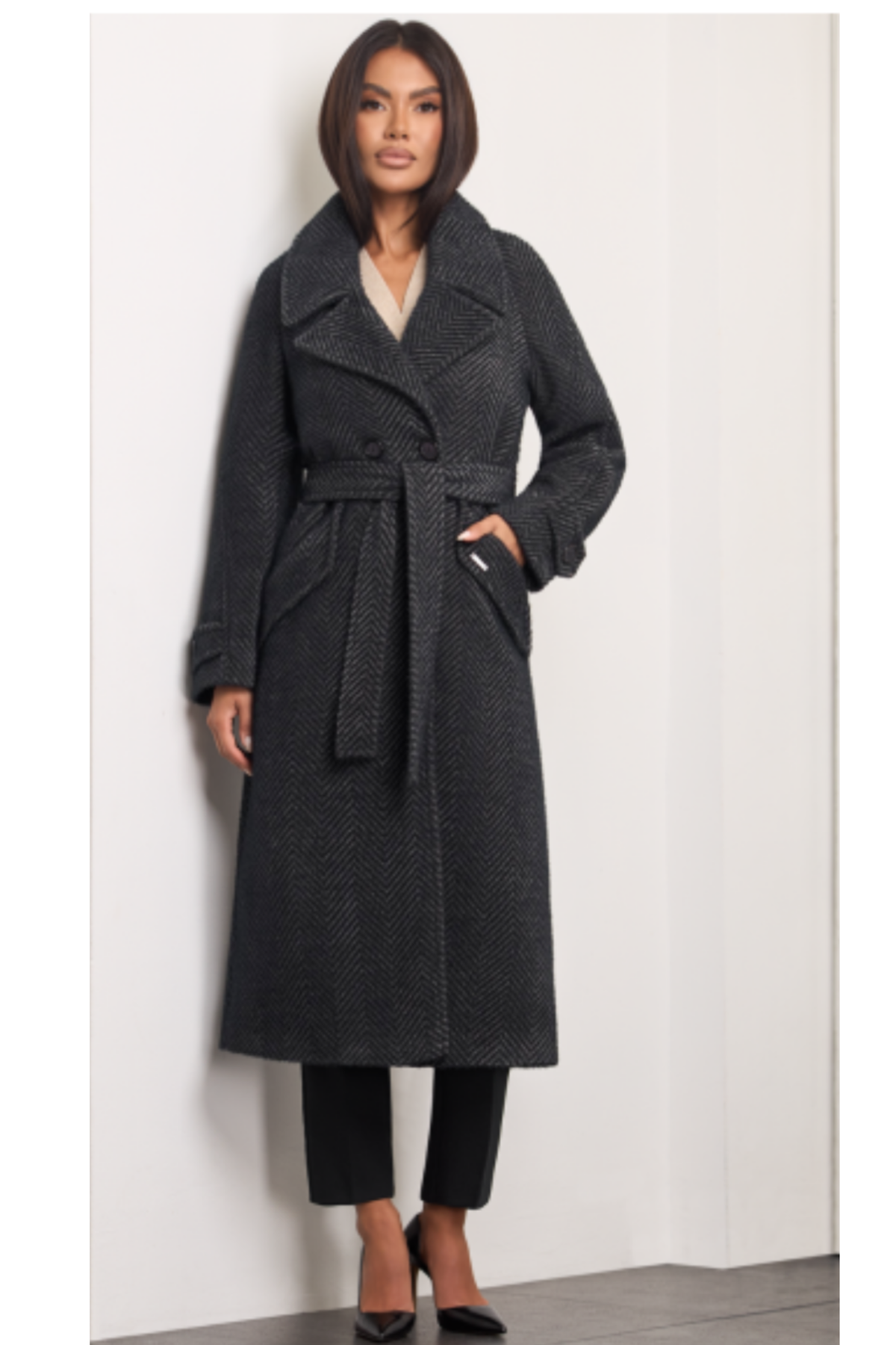 Nugat herringbone wool coat for women – long structured winter coat with double-breasted buttons, wide lapel collar, raglan sleeves, belt at the waist, flap pockets and back vent. Insulated and lined. Subtle mix of black and beige tones. Nugato spalvos moteriškas paltas su eglutės raštu – šiltas, ilgas, klasikinio silueto modelis.