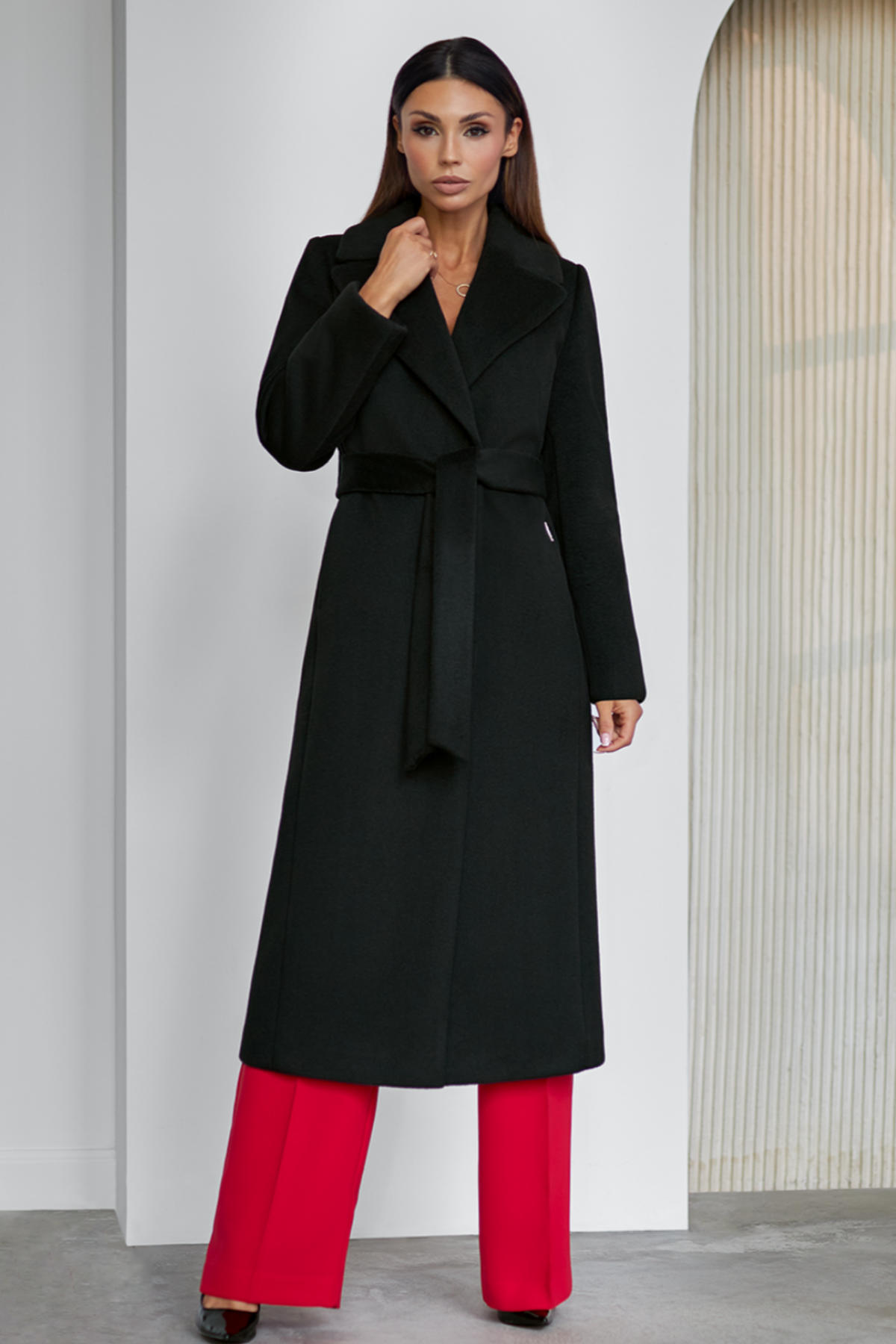 Black wool coat Amber for women – long classic winter coat with lapel collar, belt at the waist, side pockets and back vent. Elegant timeless design, insulated and lined, ideal for cold weather. Model is wearing size 34. Juodas vilnonis paltas Amber – klasikinis ilgas paltas su diržu, šoninėmis kišenėmis ir skeltuku nugaroje.