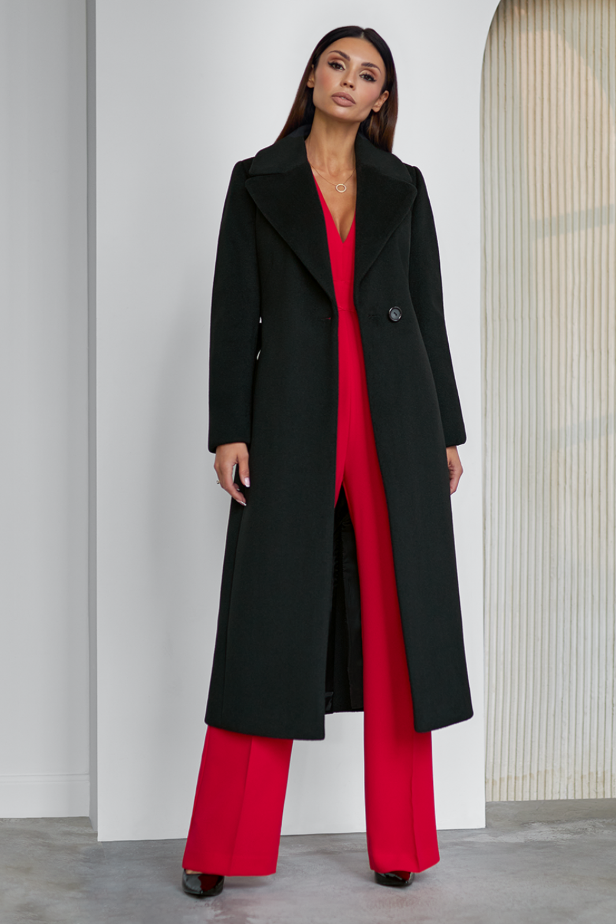 Black wool coat Amber for women – long classic winter coat with lapel collar, belt at the waist, side pockets and back vent. Elegant timeless design, insulated and lined, ideal for cold weather. Model is wearing size 34. Juodas vilnonis paltas Amber – klasikinis ilgas paltas su diržu, šoninėmis kišenėmis ir skeltuku nugaroje.
