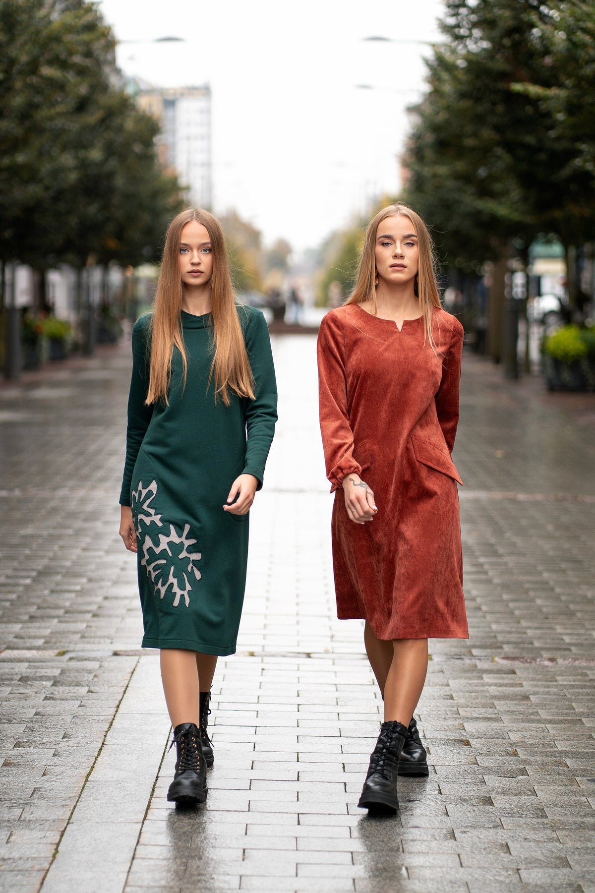Woman wearing a terracotta velvet (corduroy) dress with long sleeves gathered at the cuffs, side pockets, and a subtle neckline detail. The dress is made from a soft cotton-based fabric with fine stripes. Mid-length, breathable and elegant design for autumn and winter. / Terakotos spalvos veliūrinė suknelė su kišenėmis ir subtiliu kaklo dizainu, iš medvilninio audinio su juostelėmis.
