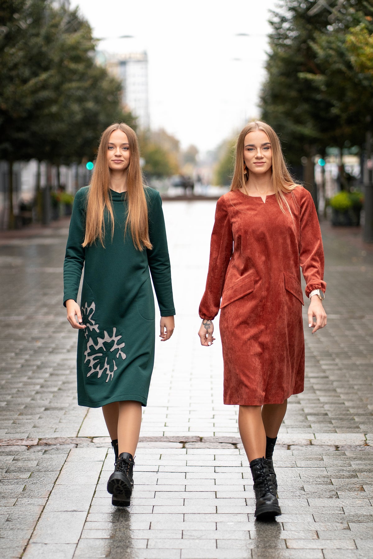 Woman wearing a terracotta velvet (corduroy) dress with long sleeves gathered at the cuffs, side pockets, and a subtle neckline detail. The dress is made from a soft cotton-based fabric with fine stripes. Mid-length, breathable and elegant design for autumn and winter. / Terakotos spalvos veliūrinė suknelė su kišenėmis ir subtiliu kaklo dizainu, iš medvilninio audinio su juostelėmis.