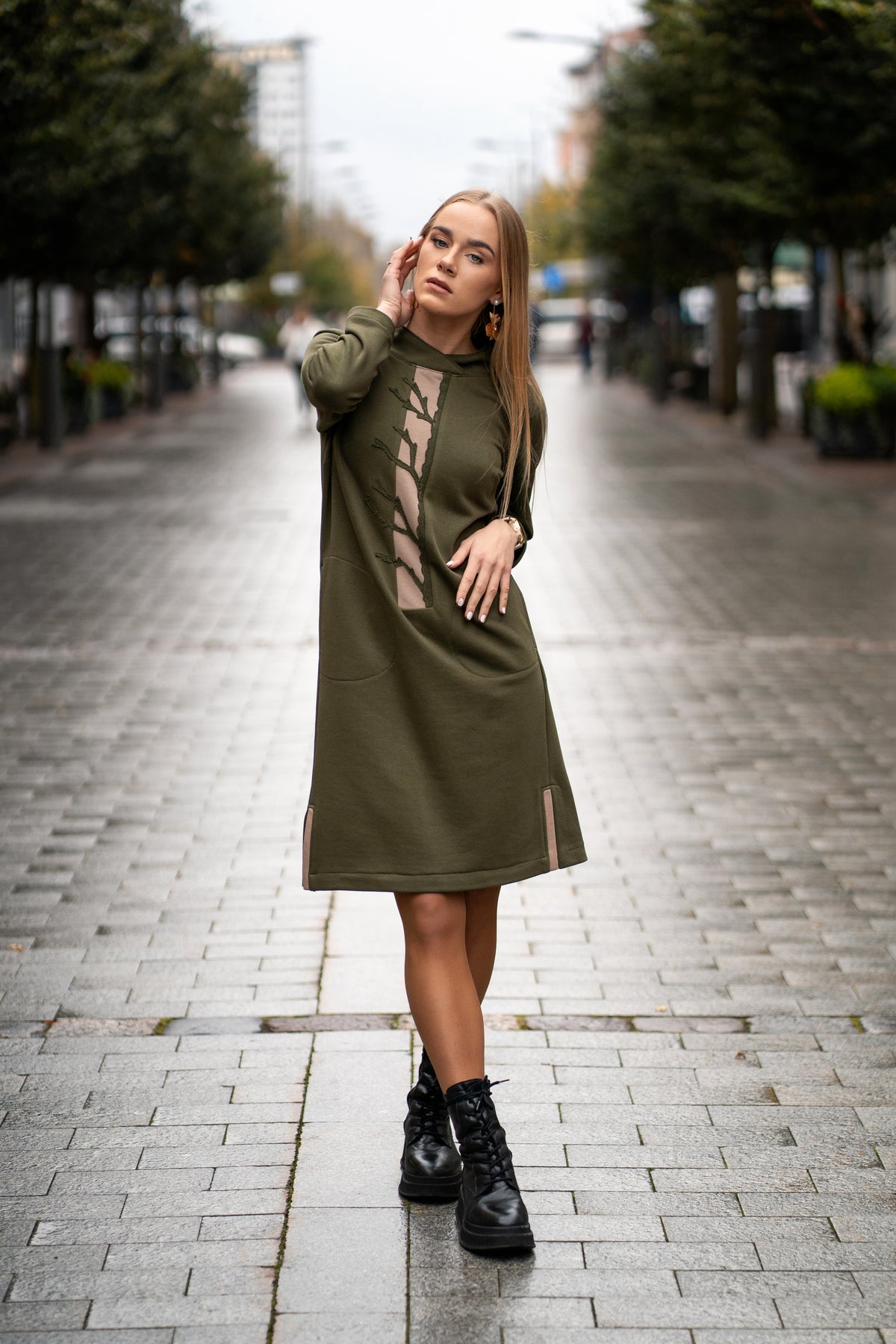 Woman wearing a moss green cotton dress with handmade tree branch embroidery on the front. The dress has long sleeves, side slits, pockets, and a straight silhouette. Comfortable medium-weight jersey fabric. / Moteris dėvi samaninės spalvos trikotažinę suknelę su rankų darbo medžio šakų dekoru, ilgomis rankovėmis, kišenėmis ir šoniniais skeltukais.
