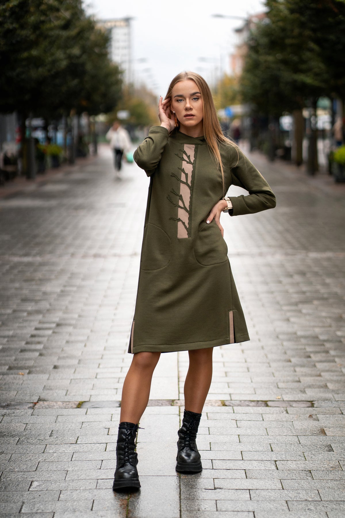 Woman wearing a moss green cotton dress with handmade tree branch embroidery on the front. The dress has long sleeves, side slits, pockets, and a straight silhouette. Comfortable medium-weight jersey fabric. / Moteris dėvi samaninės spalvos trikotažinę suknelę su rankų darbo medžio šakų dekoru, ilgomis rankovėmis, kišenėmis ir šoniniais skeltukais.