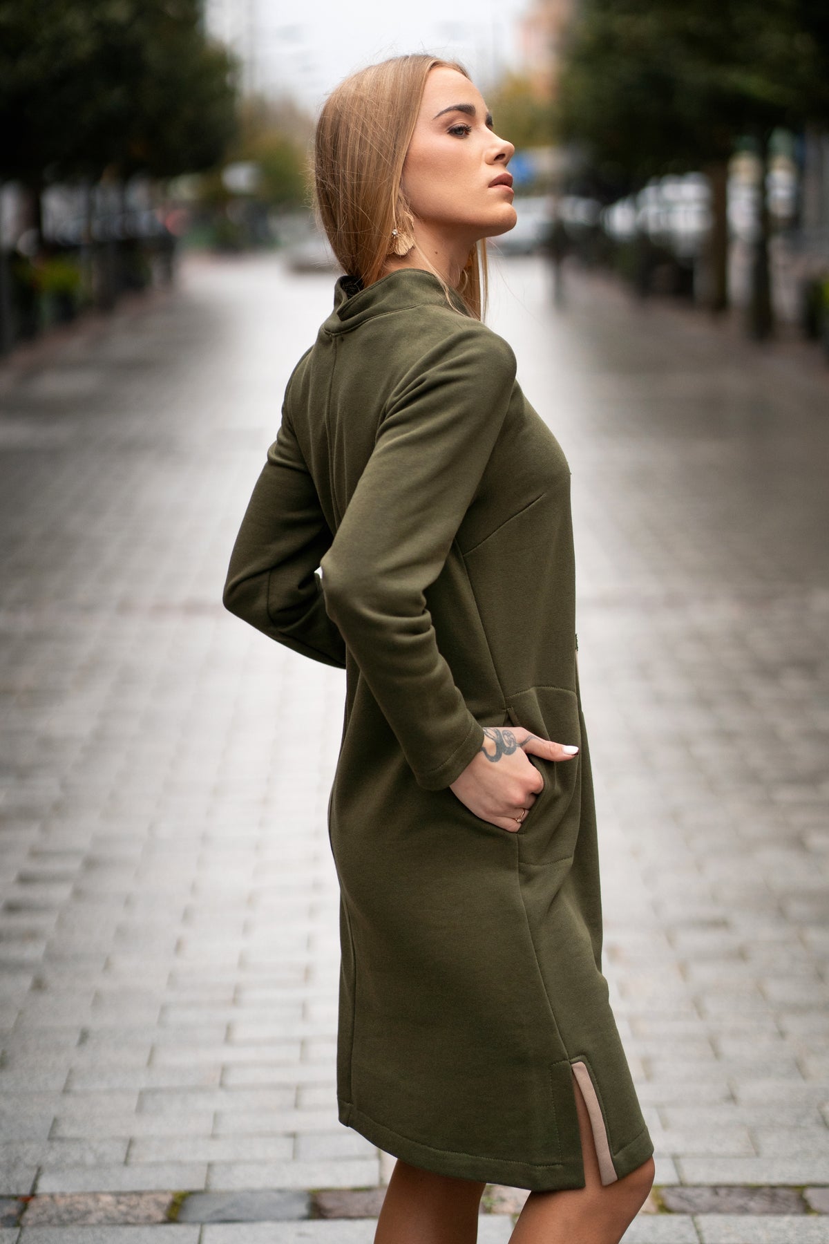 Woman wearing a moss green cotton dress with handmade tree branch embroidery on the front. The dress has long sleeves, side slits, pockets, and a straight silhouette. Comfortable medium-weight jersey fabric. / Moteris dėvi samaninės spalvos trikotažinę suknelę su rankų darbo medžio šakų dekoru, ilgomis rankovėmis, kišenėmis ir šoniniais skeltukais.
