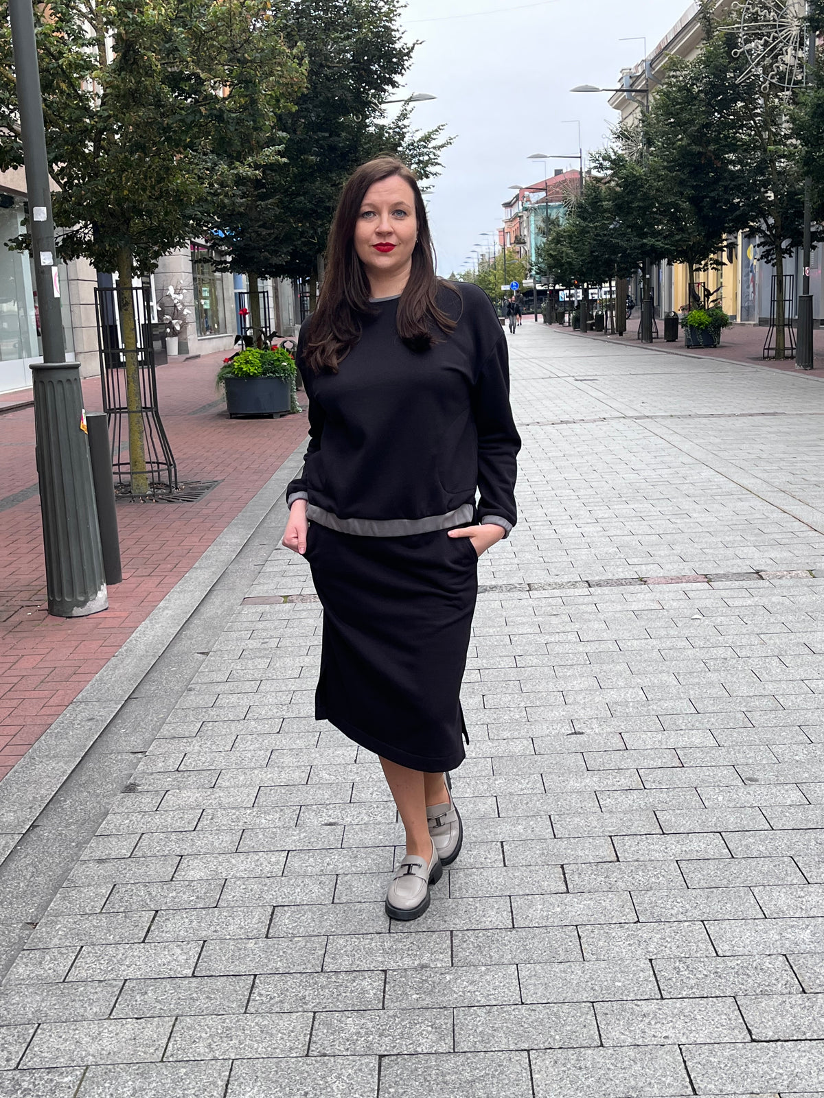 Moteriškas trikotažinis kostiumėlis iš 95 % medvilnės ir 5 % elastano. Kostiumą sudaro tiesus sijonas su guma per juosmenį, kišenėmis ir 16 cm ilgio skeltukais bei patogi palaidinė su nuleistais pečiais, kontrastingomis detalėmis, trumpesniu priekiniu kraštu ir šoniniais skeltukais. Patogus, stilingas ir siūtas Lietuvoje, dydžiai nuo 36 iki 52.
