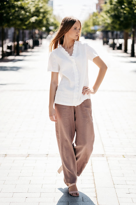 Balta lininė palaidinė moterims – trumpomis rankovėmis, dekoruota subtiliomis klostelėmis aplink kakliuką ir per priekį, siūta iš minkštinto natūralaus lino – White linen blouse for women with delicate pleated detail and short sleeves, perfect for summer wear.