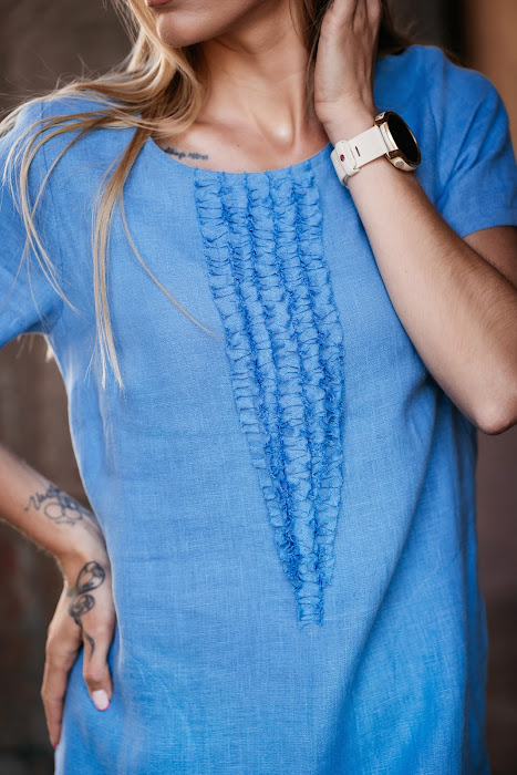 Light blue linen summer dress for women made from 100% softened linen, featuring a relaxed silhouette, short sleeves, two side pockets, and a delicate handmade-like decorative front detail. Ideal for warm weather, breathable and stylish. Modelis vilki melsvą lininę suknelę trumpomis rankovėmis, tinkamą vasarai – natūralus audinys, patogumas ir elegancija viename.