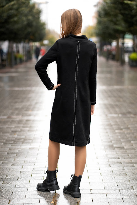 Juoda trikotažinė suknelė tiesaus silueto, su dekoratyvinėmis siūlėmis ir rankų darbo aplikacija, modelis stovi miesto gatvėje – black knit dress with decorative seams, handmade applique, straight silhouett