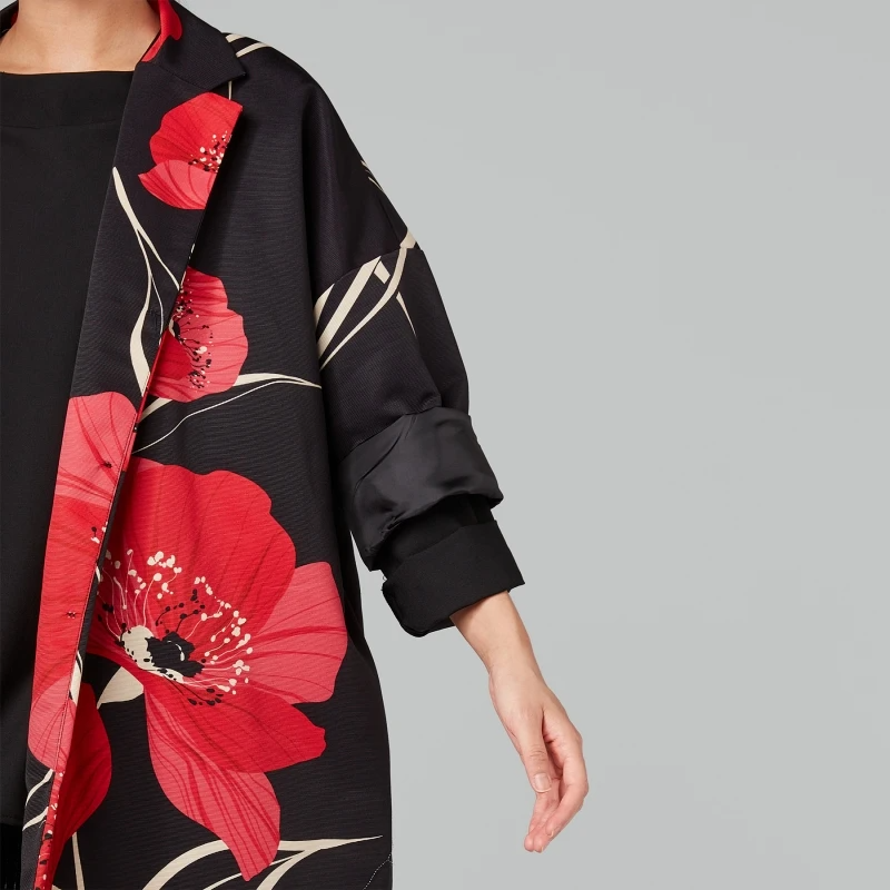 Modelis vilki kimono stiliaus juodą paltą su raudonais gėlių raštais, oversize siluetas.