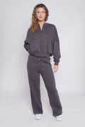 Women’s oversized loungewear set in deep grey color, featuring a zip-up sweatshirt with ribbed cuffs and wide-leg high-waisted pants with a drawstring. Soft cotton blend fabric with a gentle inner fleece. Comfortable casual outfit for everyday wear. Moteriškas oversize laisvalaikio kostiumas su džemperiu ir platėjančiomis kelnėmis