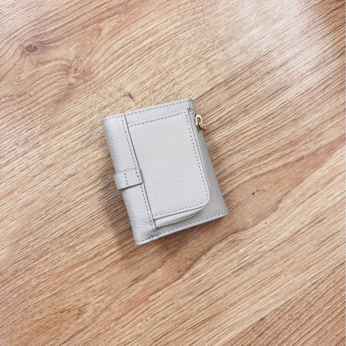 Elegantiška pilka moteriška piniginė iš natūralios odos su auksinės spalvos furnitūra ir užsegimu. Kompaktiškas dydis 8x10x2,5 cm leidžia patogiai laikyti pinigus visu ilgiu, dokumentus, banko bei nuolaidų korteles. Monetoms skirtas skyrelis su užtrauktuku suteikia papildomo patogumo. Piniginė yra maža, bet labai talpi, todėl lengvai telpa net ir mažoje rankinėje. Tai stilingas, praktiškas ir ilgaamžis aksesuaras, puikiai tinkantis kasdieniam naudojimui ar kaip dovanų idėja.